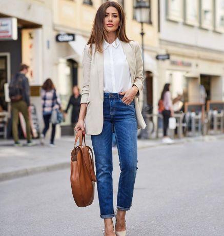 Woman wearing a timeless minimalist outfit with a white shirt, beige blazer, and classic blue jeans.